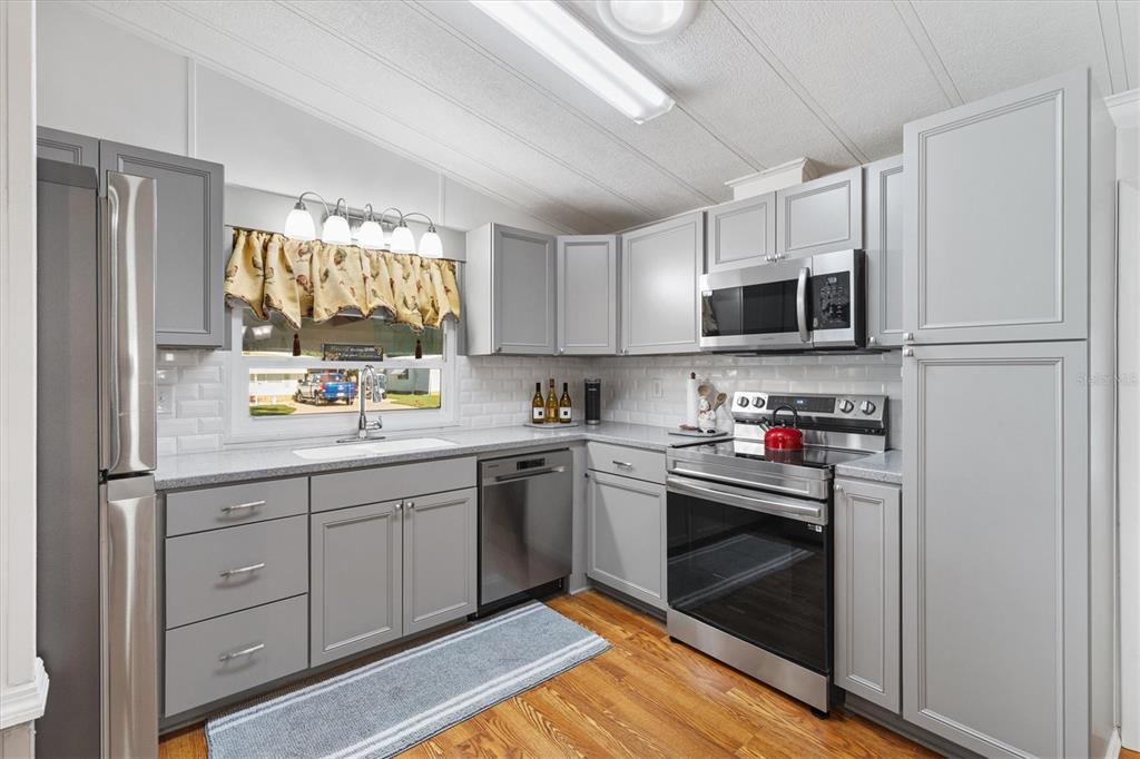 A kitchen features gray cabinets, stainless steel appliances, white subway tile backsplash, and wood flooring — 732 ROYAL PALM AVENUE, LADY LAKE, FL
