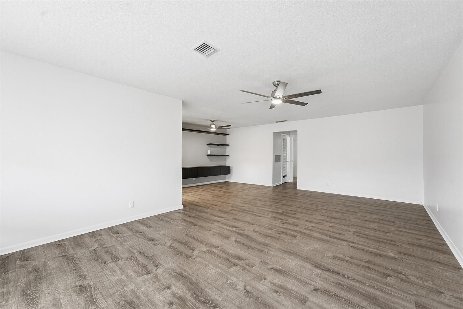 An empty living room features white walls, wood-look flooring, two ceiling fans, and built-in shelving — 355 Main Boulevard # C, Boynton Beach FL 33435, BOYNTON BEACH, FL