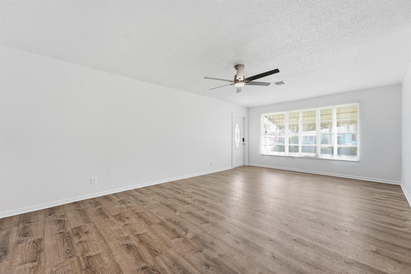 An empty living room features white walls, wood-look flooring, a ceiling fan, and large windows — 355 Main Boulevard # C, Boynton Beach FL 33435, BOYNTON BEACH, FL
