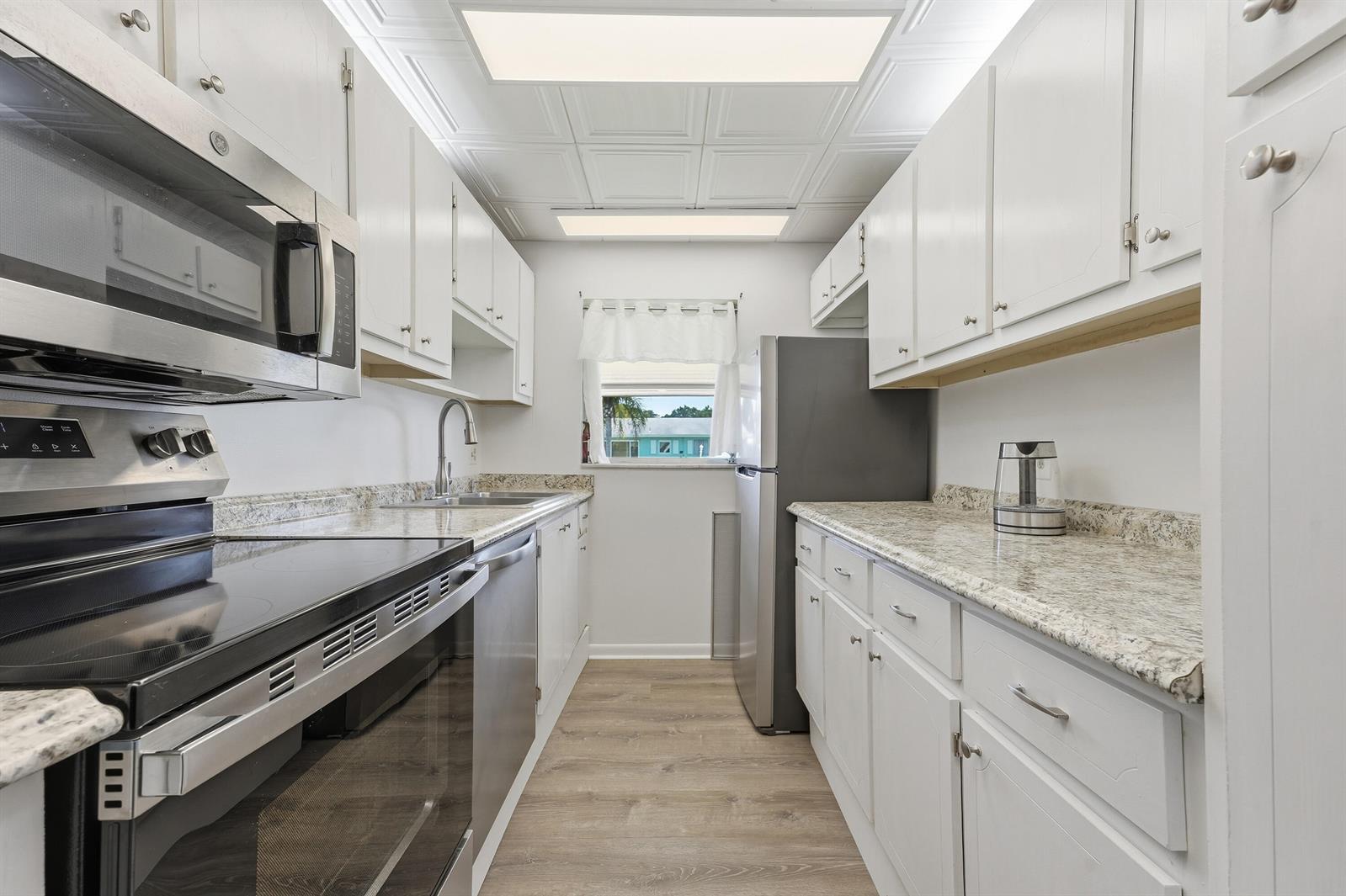 A galley kitchen features white cabinets, stainless steel appliances, and granite countertops — 355 Main Boulevard # C, Boynton Beach FL 33435, BOYNTON BEACH, FL