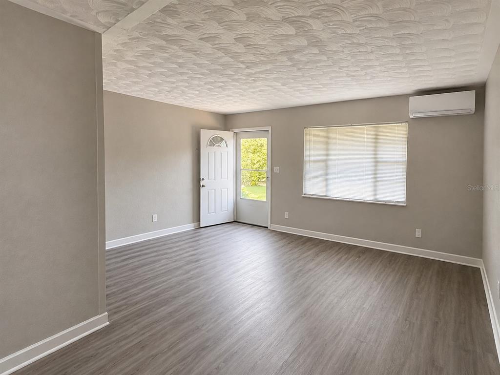 An empty living room features gray wood-look flooring, light gray walls, and a textured ceiling — 1044 58TH AVENUE N, ST PETERSBURG, FL