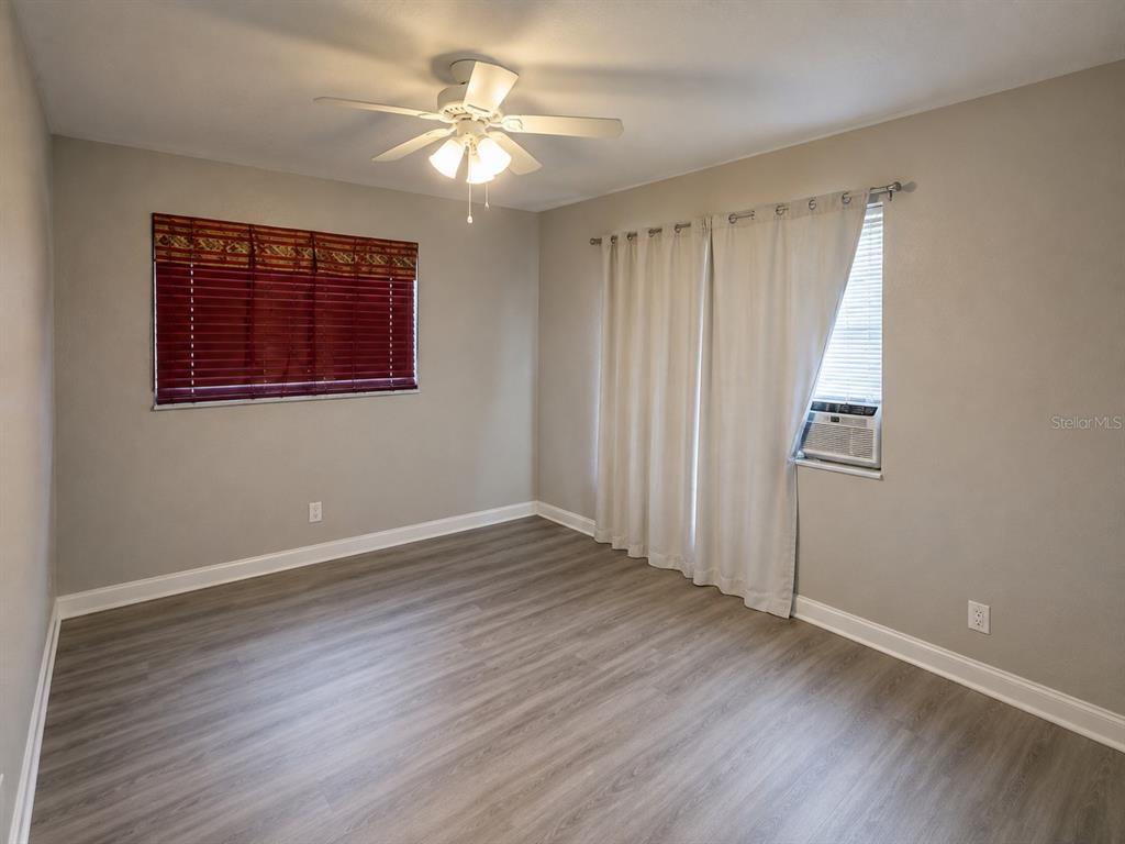 An empty bedroom features light gray walls, wood-look flooring, a ceiling fan, and window treatments — 1044 58TH AVENUE N, ST PETERSBURG, FL