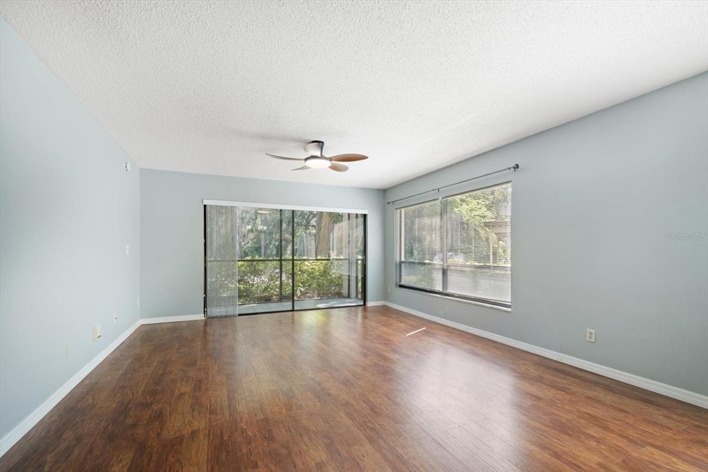 An empty living room features light blue walls, wood-look flooring, a ceiling fan, and large windows — 700 STARKEY ROAD UNIT 1111, LARGO, FL