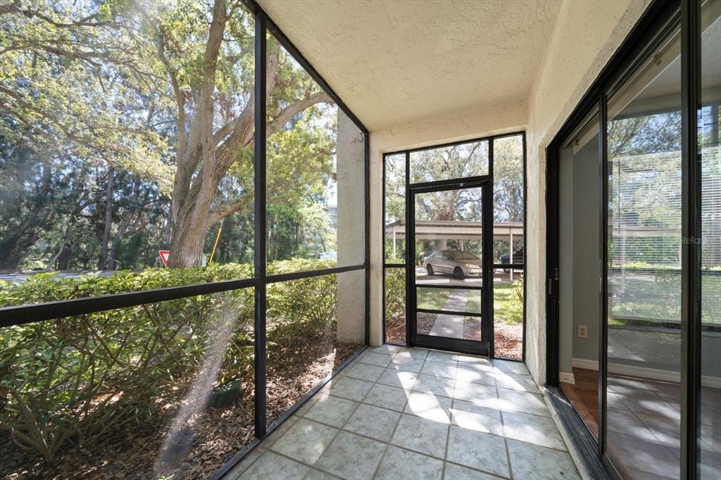 A screened-in porch with tiled flooring overlooks a parking area and trees — 700 STARKEY ROAD UNIT 1111, LARGO, FL