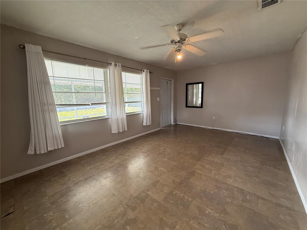 An empty living room features tile flooring, a ceiling fan, and two windows with curtains — 2402 9TH STREET E, BRADENTON, FL
