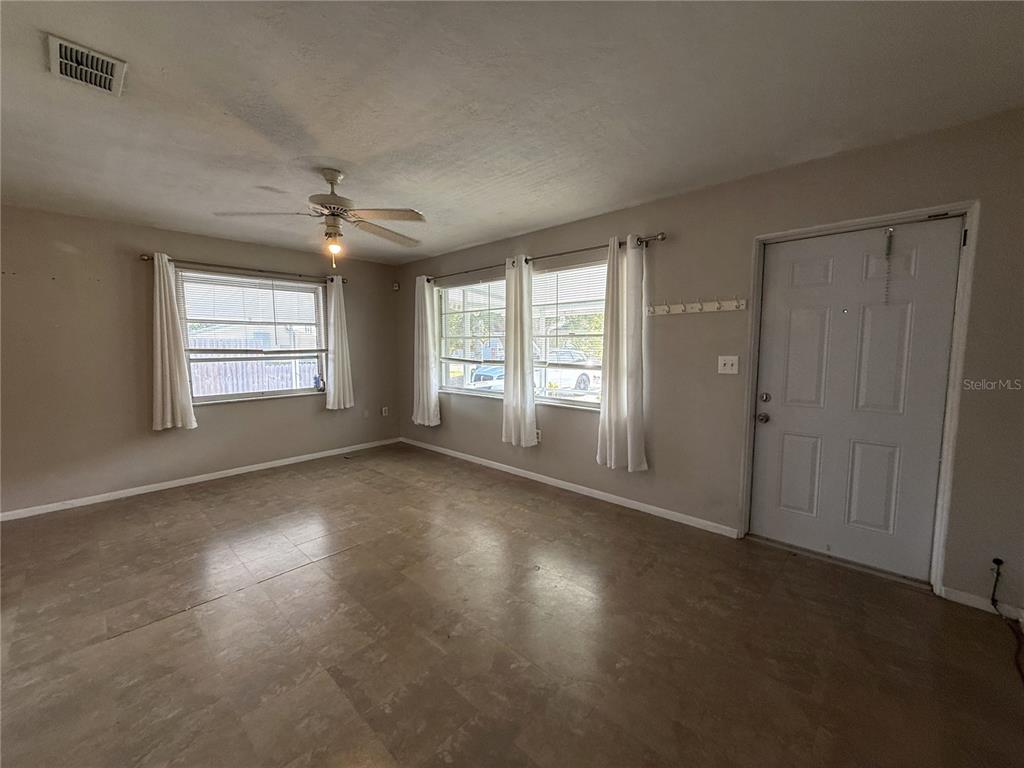 An empty living room features light-colored walls, tile flooring, a ceiling fan, and white curtains — 2402 9TH STREET E, BRADENTON, FL