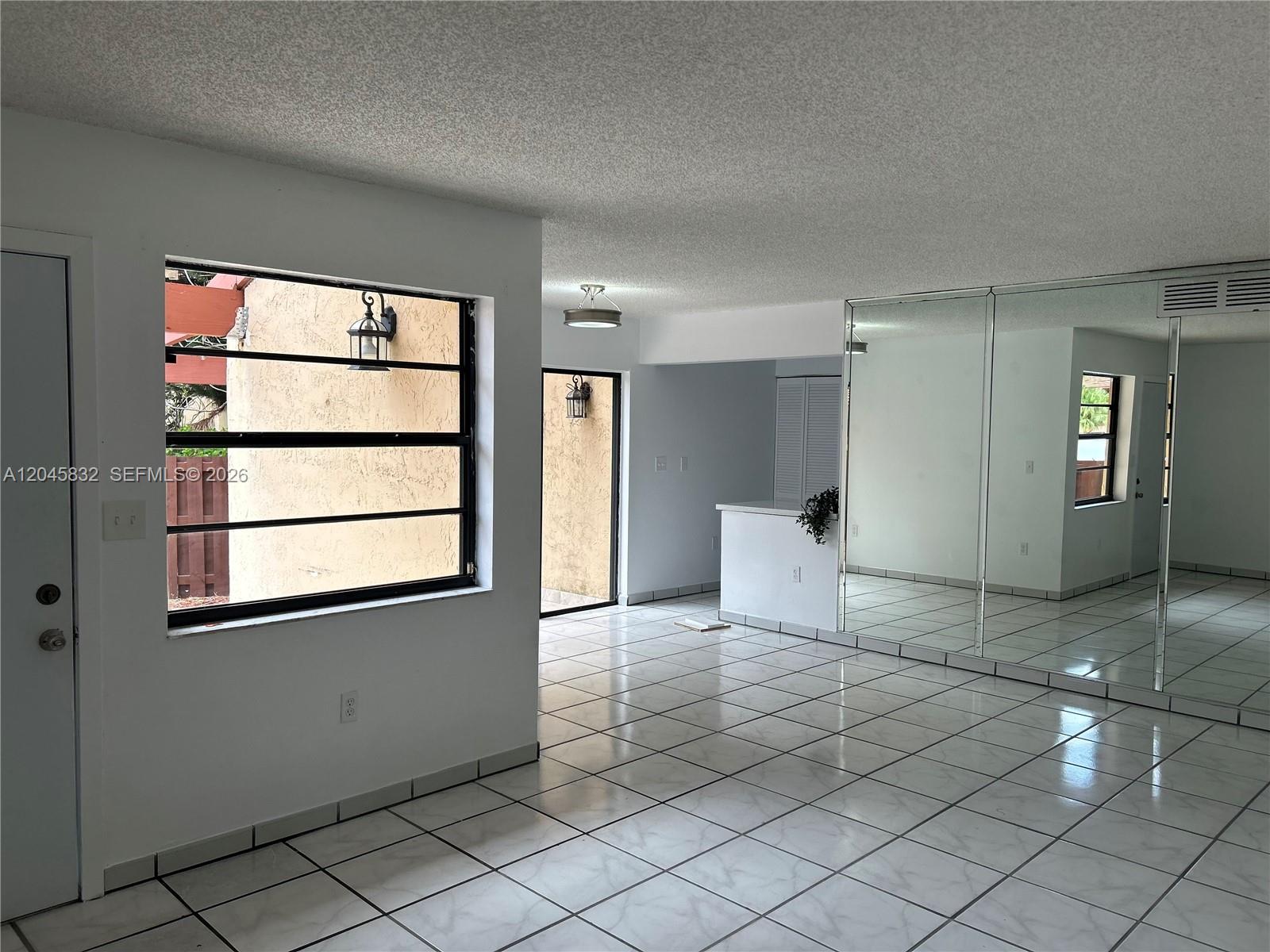 An interior room features white tile flooring, mirrored closet doors, and a large window — 301 W Park Dr # 11, Miami FL 33172, MIAMI, FL