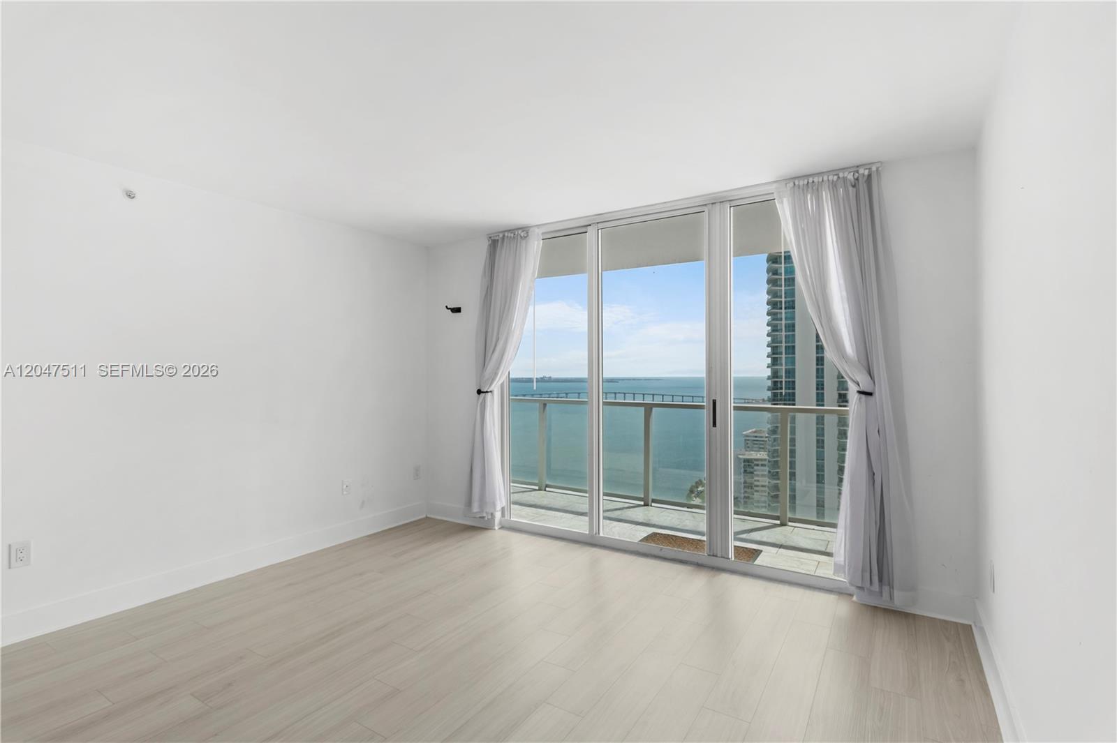 An empty room with light wood flooring and floor-to-ceiling windows overlooking the ocean — 1155 Brickell Bay Dr # 3105, Miami FL 33131, MIAMI, FL