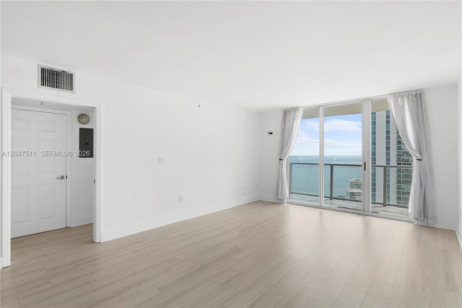 An empty room with light wood flooring, white walls, and a balcony overlooking the ocean — 1155 Brickell Bay Dr # 3105, Miami FL 33131, MIAMI, FL