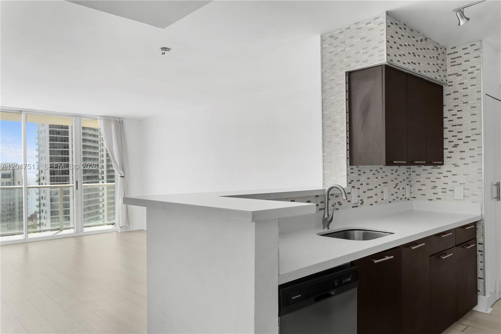 A kitchen with dark cabinets and white countertops overlooks an empty living area with balcony — 1155 Brickell Bay Dr # 3105, Miami FL 33131, MIAMI, FL