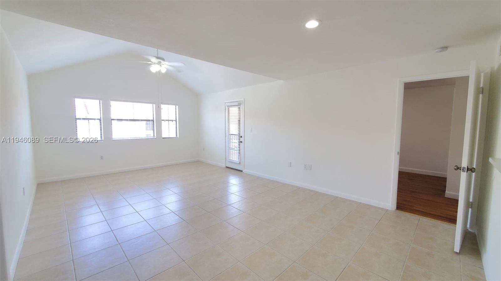 An empty living room features vaulted ceilings, tile flooring, a ceiling fan, and a glass door — 10500 SW 155th Ct # 1022, Miami FL 33196, MIAMI, FL