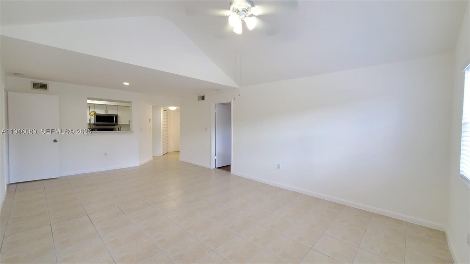 A bright, tiled living room features a vaulted ceiling, a ceiling fan, and a pass-through kitchen — 10500 SW 155th Ct # 1022, Miami FL 33196, MIAMI, FL