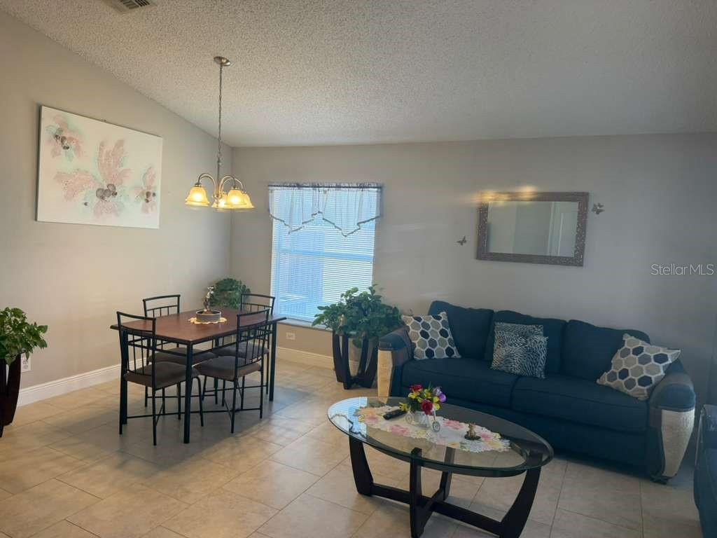 A dining area and living room with tile floors, a blue sofa, and a table — 1702 MINNOW COURT, KISSIMMEE, FL