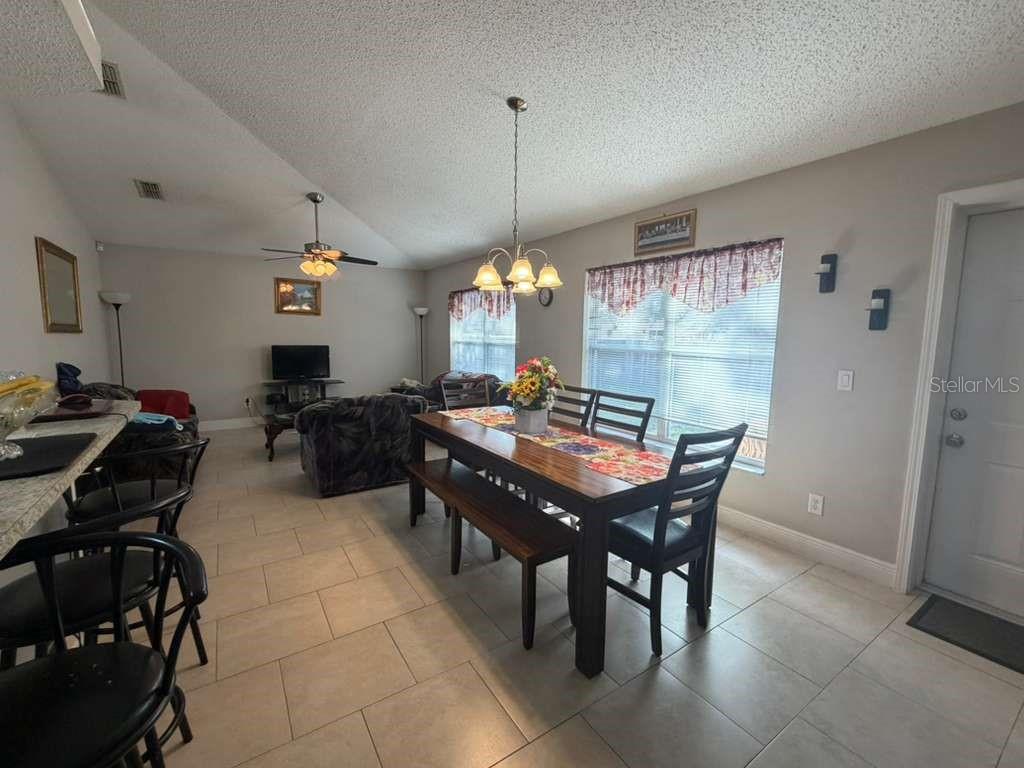 An open-concept living and dining area features tile flooring, a vaulted ceiling, and neutral walls — 1702 MINNOW COURT, KISSIMMEE, FL