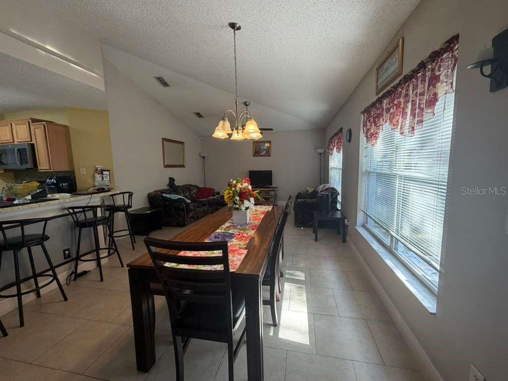 A dining area with a long wooden table, tile flooring, and an adjacent kitchen counter — 1702 MINNOW COURT, KISSIMMEE, FL