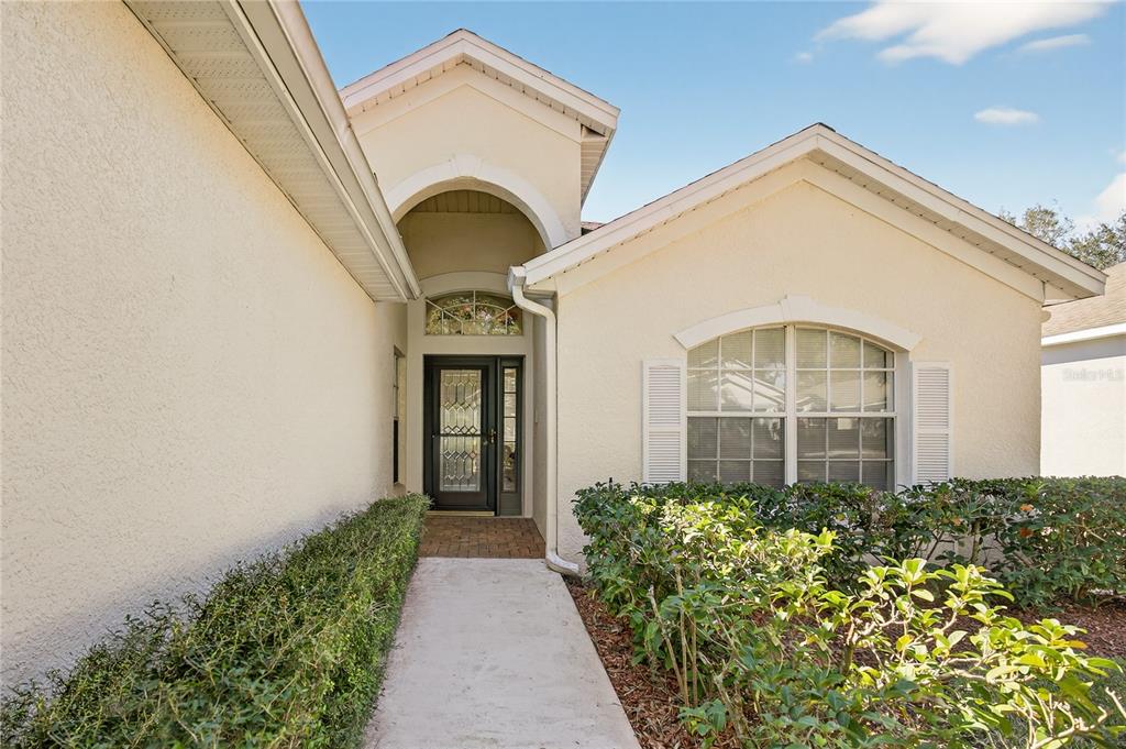 A concrete walkway leads to the front entrance of a beige house with arched windows — 3786 AVON COURT, CLERMONT, FL