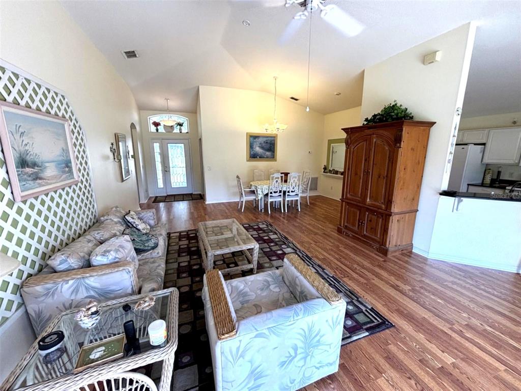 A living room and dining area with vaulted ceilings, wood flooring, and wicker furniture — 3786 AVON COURT, CLERMONT, FL