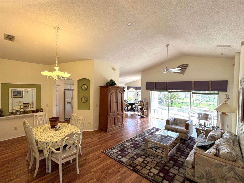 A living and dining area features wood-look flooring, a vaulted ceiling, and sliding glass doors — 3786 AVON COURT, CLERMONT, FL