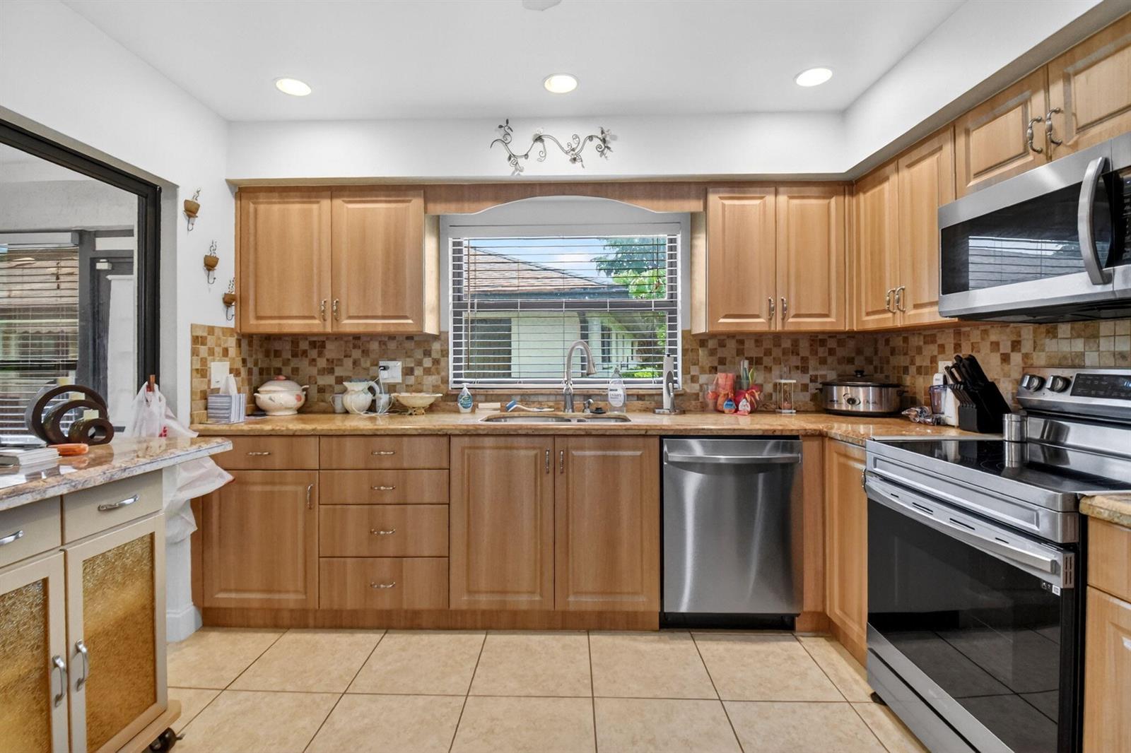 A kitchen features light wood cabinets, stainless steel appliances, a tiled backsplash, and tile flooring — 4735 Quailwood Way # A, Boynton Beach FL 33436, BOYNTON BEACH, FL