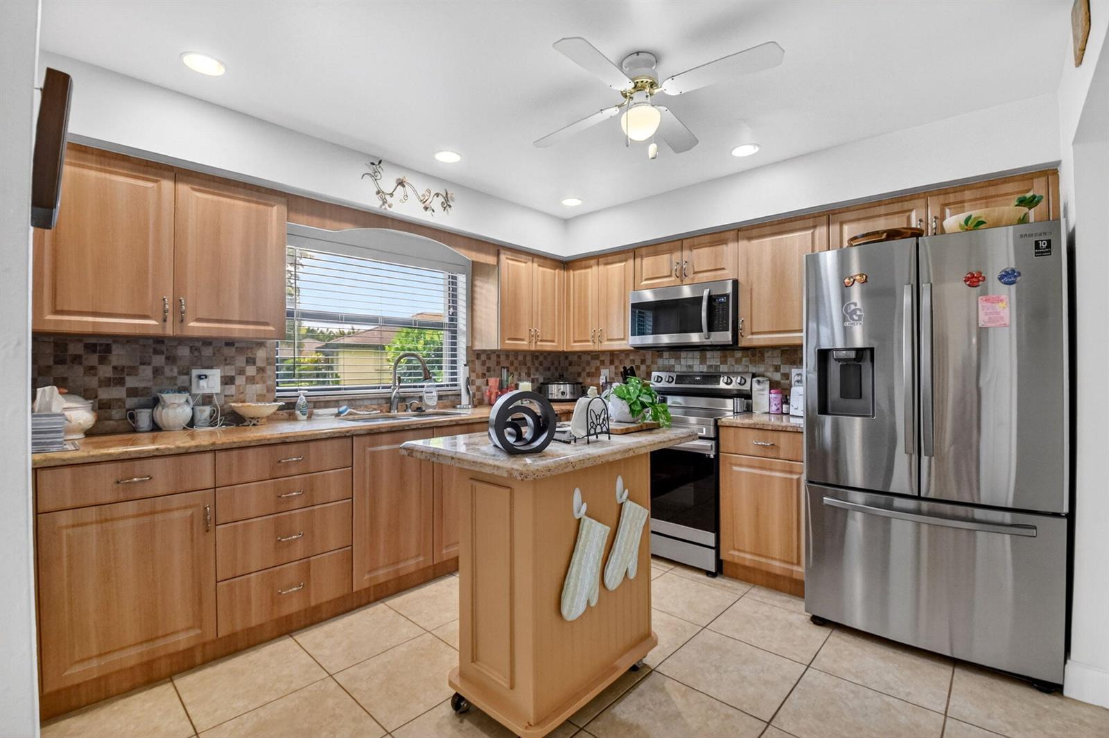 A kitchen features light wood cabinets, granite countertops, stainless steel appliances, and a rolling island — 4735 Quailwood Way # A, Boynton Beach FL 33436, BOYNTON BEACH, FL