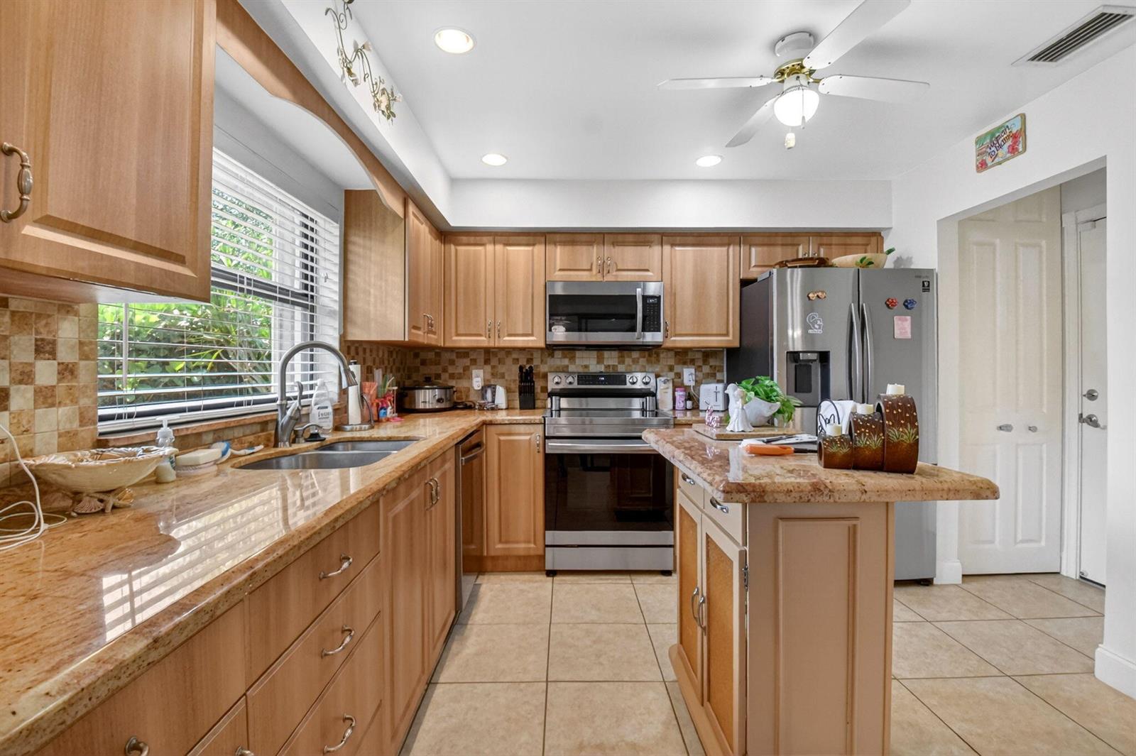 A kitchen features light wood cabinets, granite countertops, stainless steel appliances, and tile flooring — 4735 Quailwood Way # A, Boynton Beach FL 33436, BOYNTON BEACH, FL