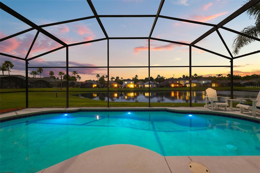 A swimming pool with a screened enclosure overlooks a lake at sunset — 948 LAKE BERKLEY DRIVE, KISSIMMEE, FL