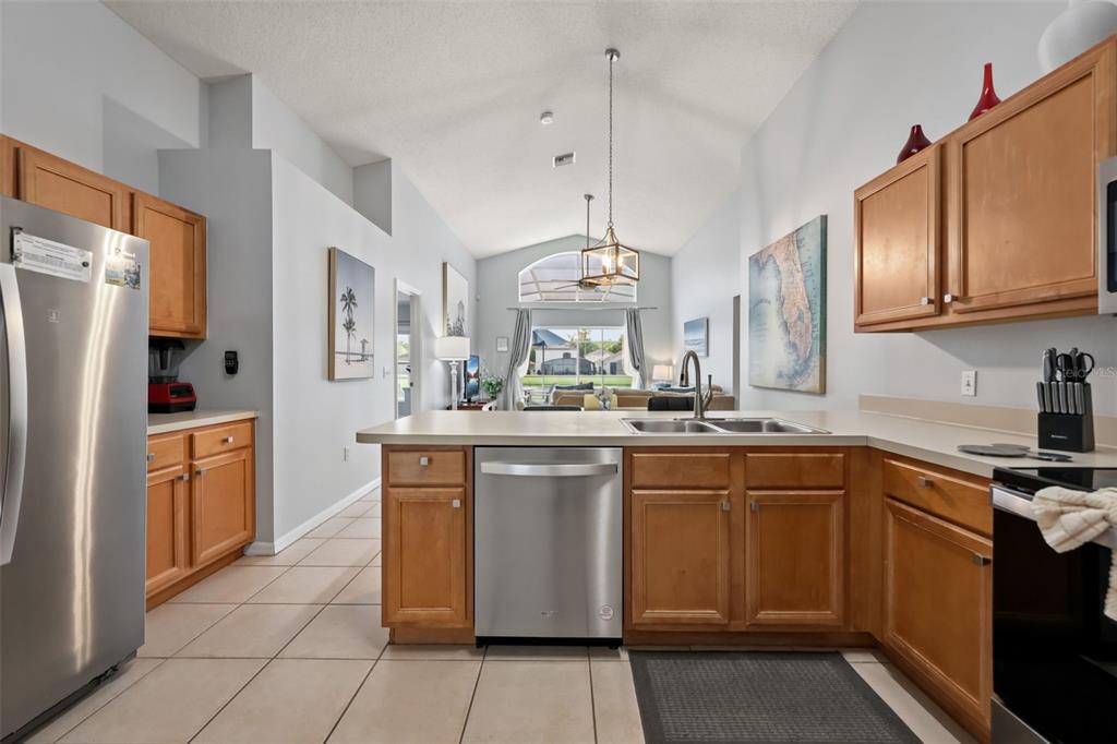 A kitchen with wood cabinets, stainless steel appliances, and a view into the living area — 948 LAKE BERKLEY DRIVE, KISSIMMEE, FL