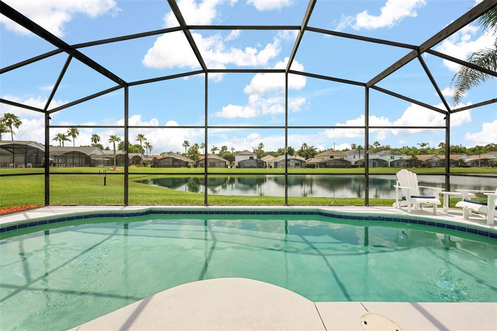 A swimming pool enclosed by a screen cage overlooks a lake and residential neighborhood — 948 LAKE BERKLEY DRIVE, KISSIMMEE, FL