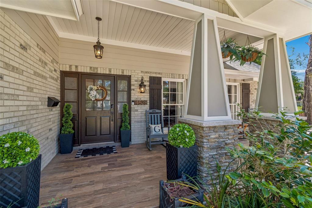 A front porch with a wood-look floor, stone columns, and a dark wood front door — 4528 W WOODMERE ROAD, TAMPA, FL
