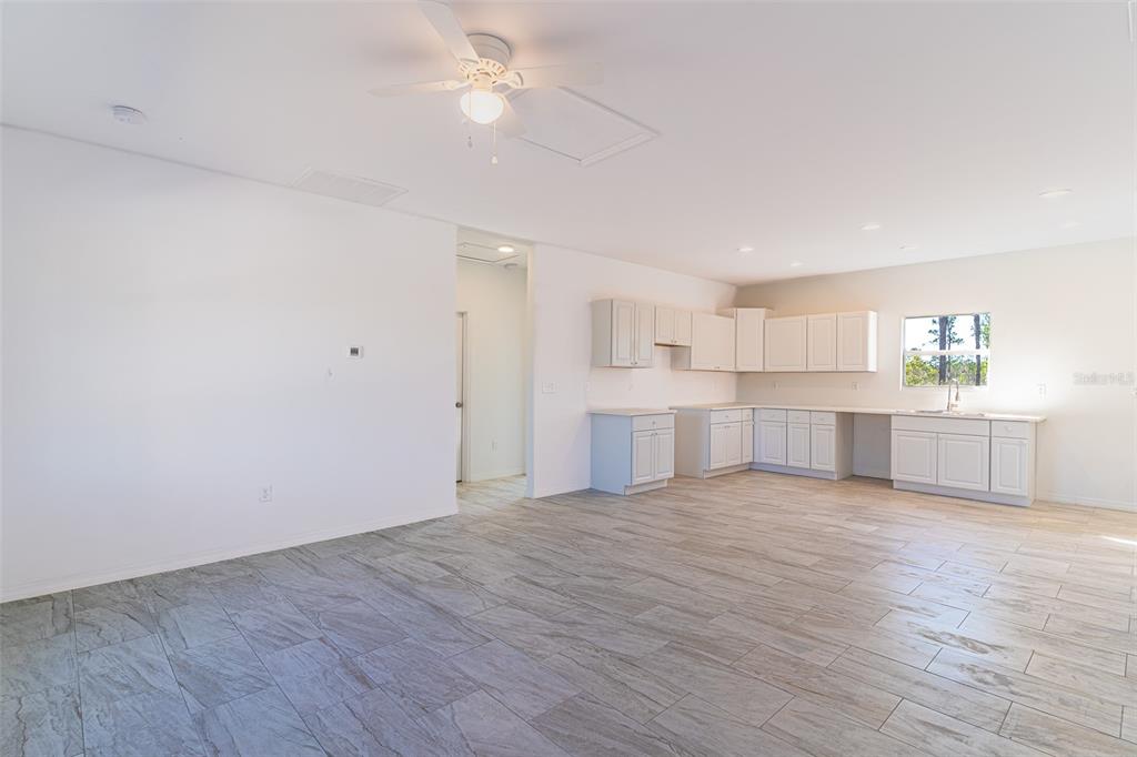 An open-concept kitchen and living area features white cabinets, tile flooring, and a ceiling fan — 1407 BITTERSWEET STREET, LAKE PLACID, FL
