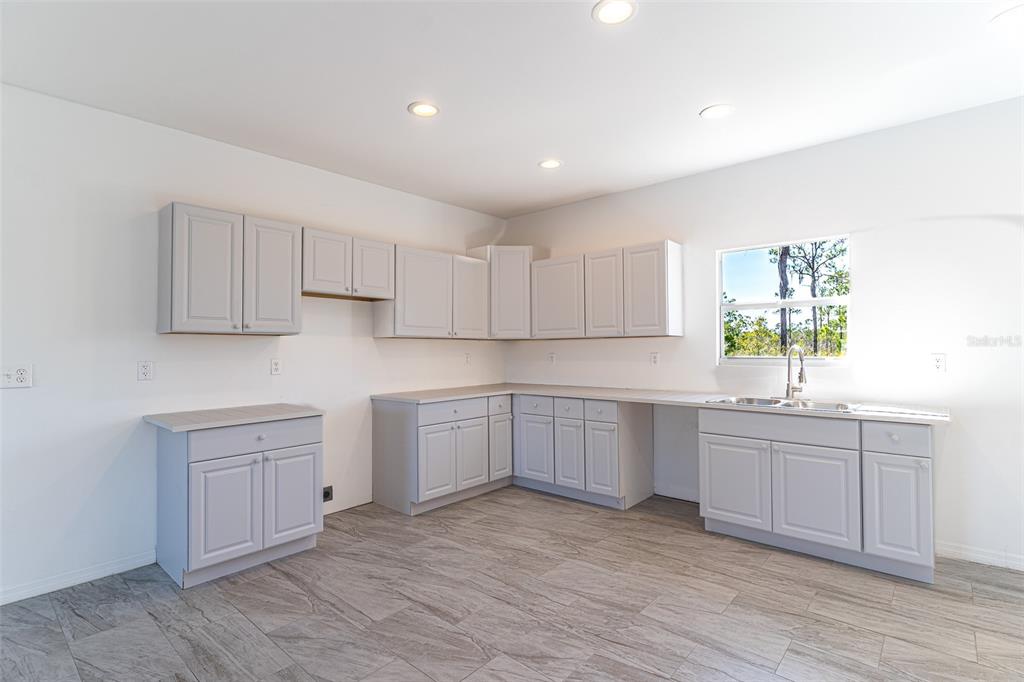 A kitchen features light gray cabinets, light countertops, and wood-look tile flooring — 1407 BITTERSWEET STREET, LAKE PLACID, FL