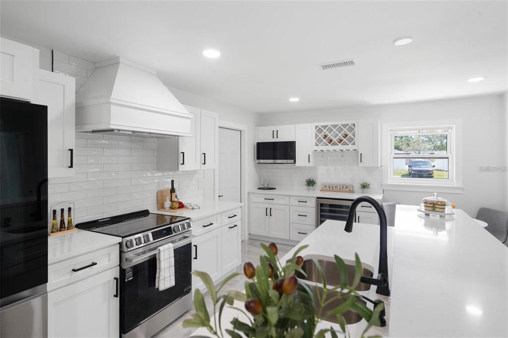 A modern white kitchen features a large island, stainless steel appliances, and black hardware — 1715 DELAWARE AVENUE NE, ST PETERSBURG, FL