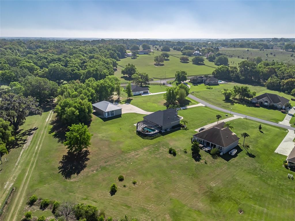 An aerial view shows several houses with pools and garages situated on a large grassy lot — 13945 SE 156TH LANE, WEIRSDALE, FL