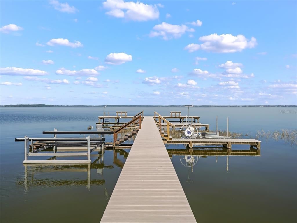 A long wooden dock extends into a calm lake under a blue sky with clouds — 13945 SE 156TH LANE, WEIRSDALE, FL