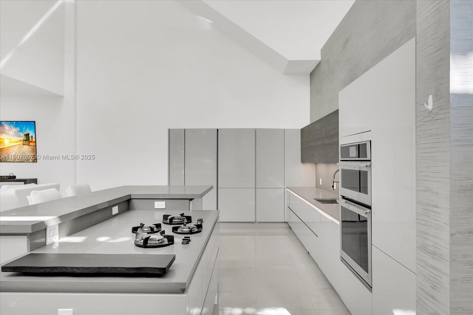 A modern kitchen features a central island with a gas cooktop and white cabinetry — 7830 Atlantic Way, Miami Beach FL 33141, MIAMI BEACH, FL