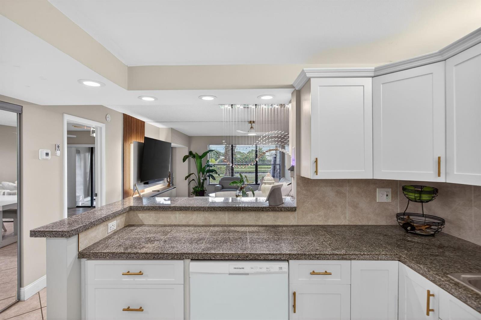 A kitchen with white cabinets, granite countertops, and a pass-through window overlooking the living area — 2314 S Cypress Bend Drive # 114, Pompano Beach FL 33069, POMPANO BEACH, FL