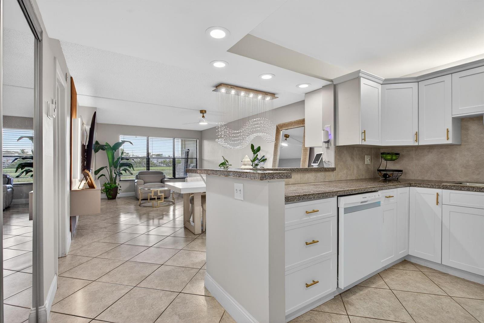 A kitchen with white cabinets and granite countertops overlooks a dining area with tile floors — 2314 S Cypress Bend Drive # 114, Pompano Beach FL 33069, POMPANO BEACH, FL