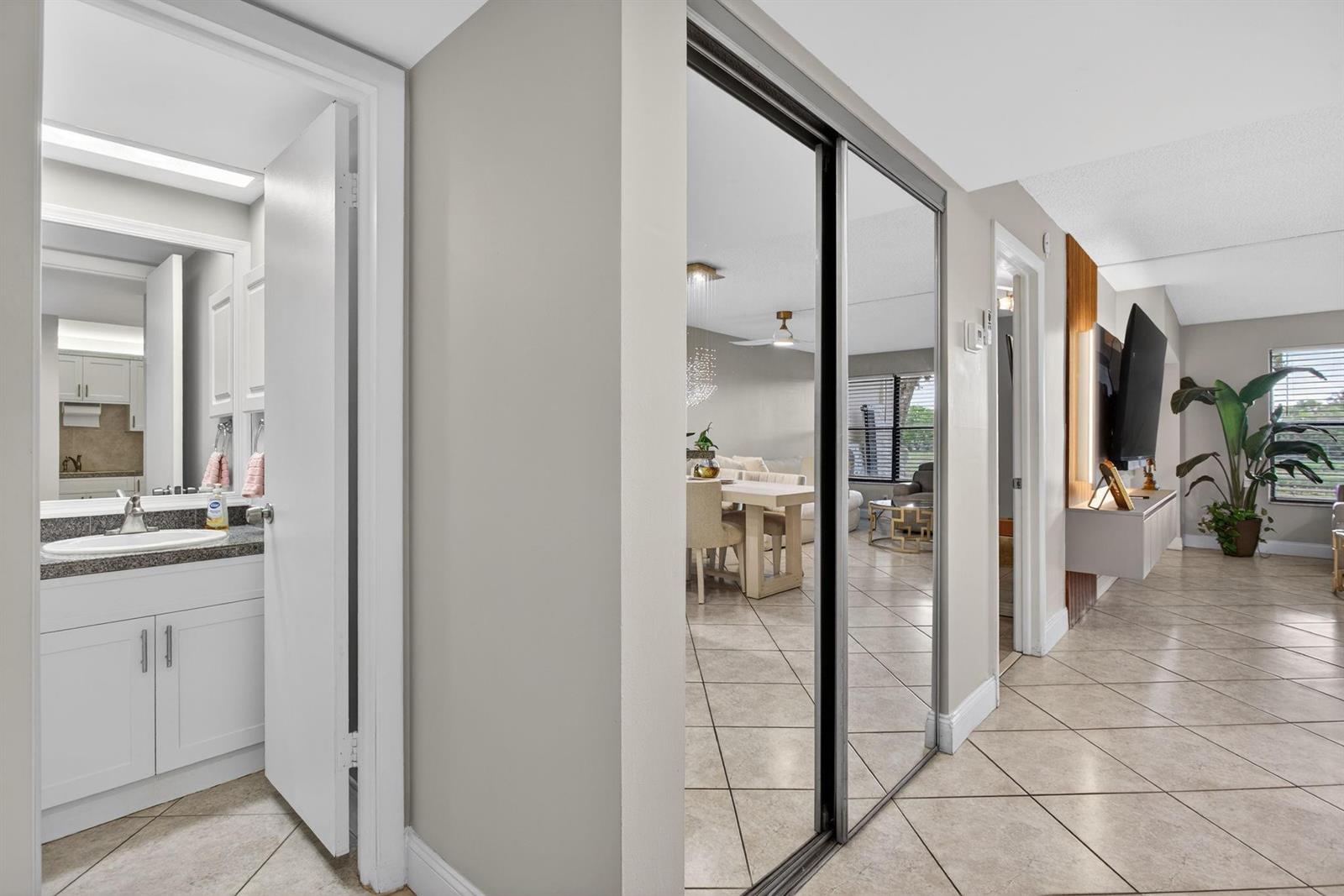 A hallway features a bathroom entrance, mirrored closet doors, and tile flooring leading to a living area — 2314 S Cypress Bend Drive # 114, Pompano Beach FL 33069, POMPANO BEACH, FL
