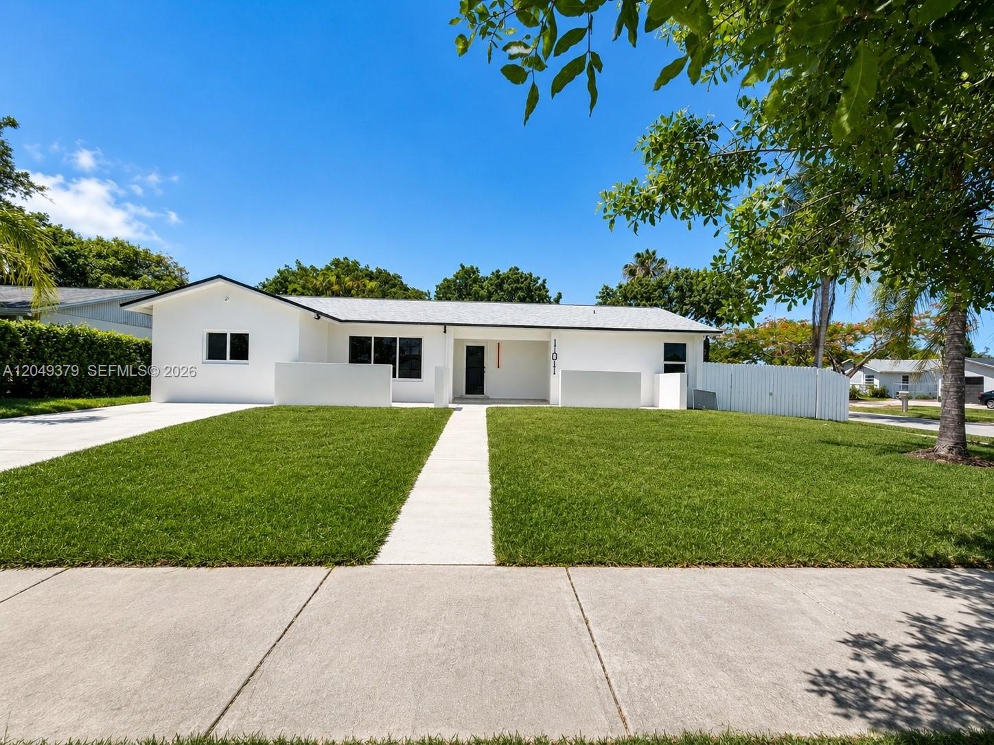 A single-story white house with a flat roof and a front lawn under blue sky — 11011 SW 162nd Ter, Miami FL 33157, MIAMI, FL