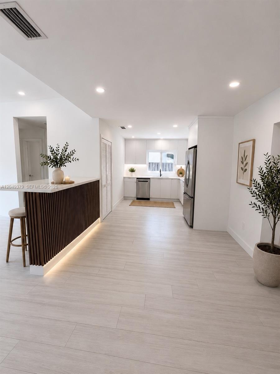 A modern kitchen features white cabinetry, stainless steel appliances, and a slatted wood breakfast bar — 11011 SW 162nd Ter, Miami FL 33157, MIAMI, FL