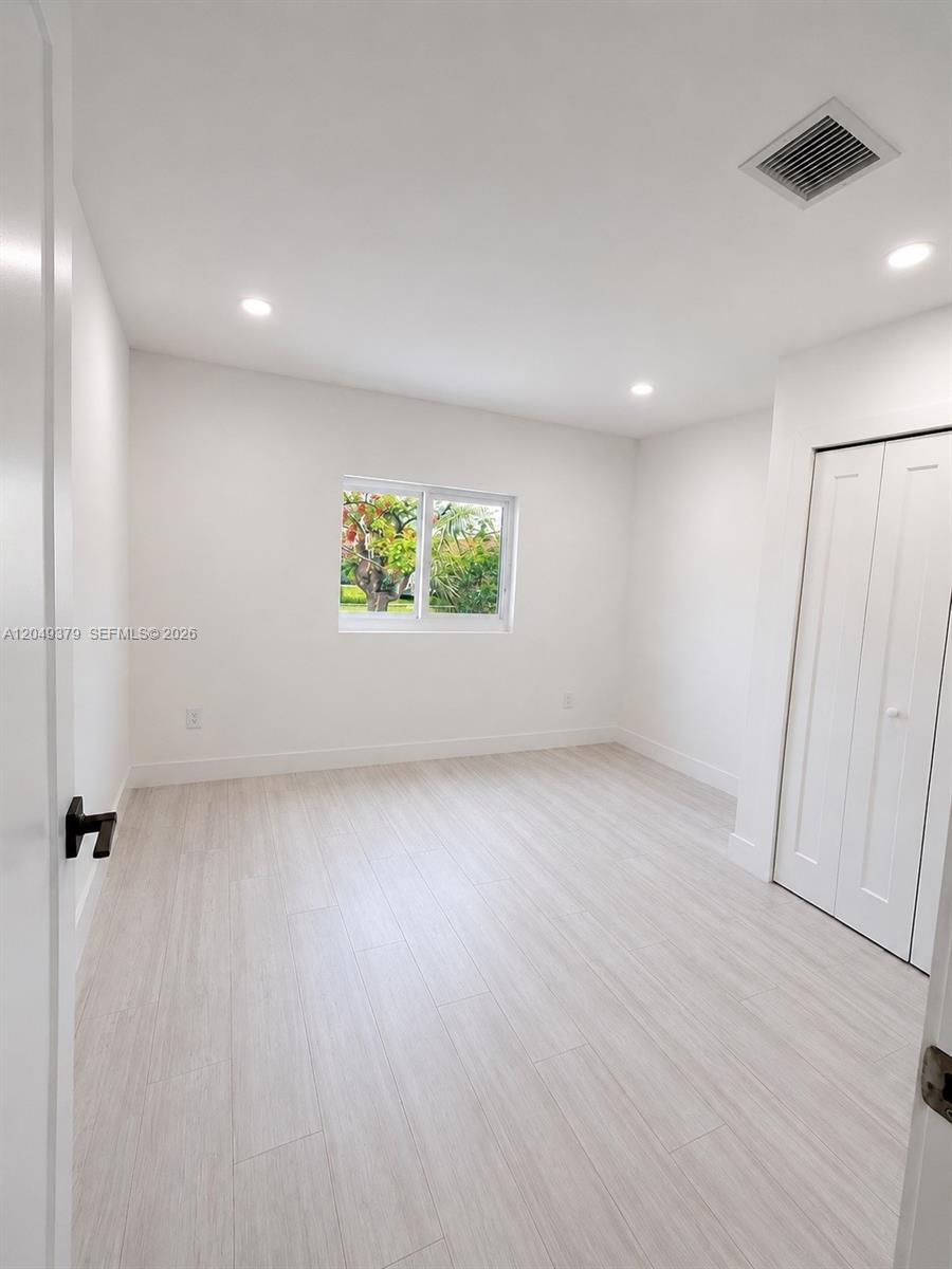 A bright, empty bedroom features light wood-look flooring, white walls, and a sliding closet door — 11011 SW 162nd Ter, Miami FL 33157, MIAMI, FL