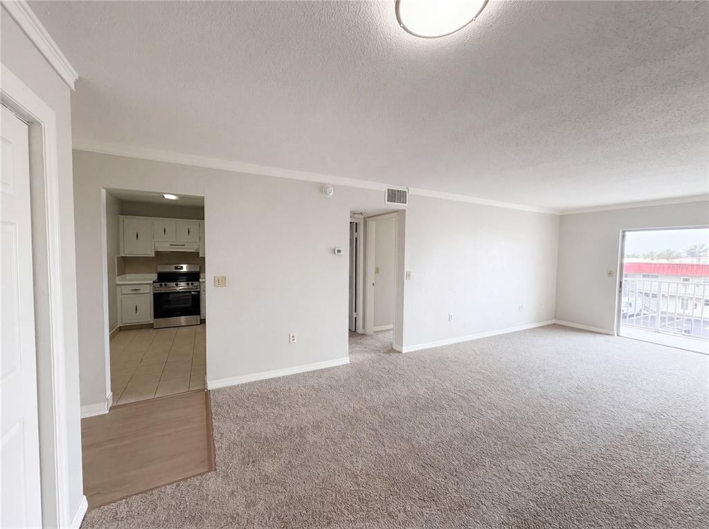 A living room with carpeted flooring leads to a kitchen and a balcony — 2711 N HALIFAX AVENUE UNIT 371, DAYTONA BEACH, FL