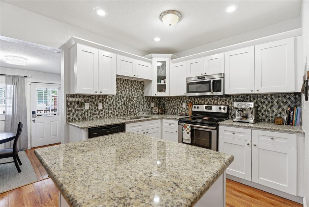 A kitchen features white cabinets, granite countertops, a patterned tile backsplash, and stainless steel appliances — 3017 N WOODROW AVENUE, TAMPA, FL
