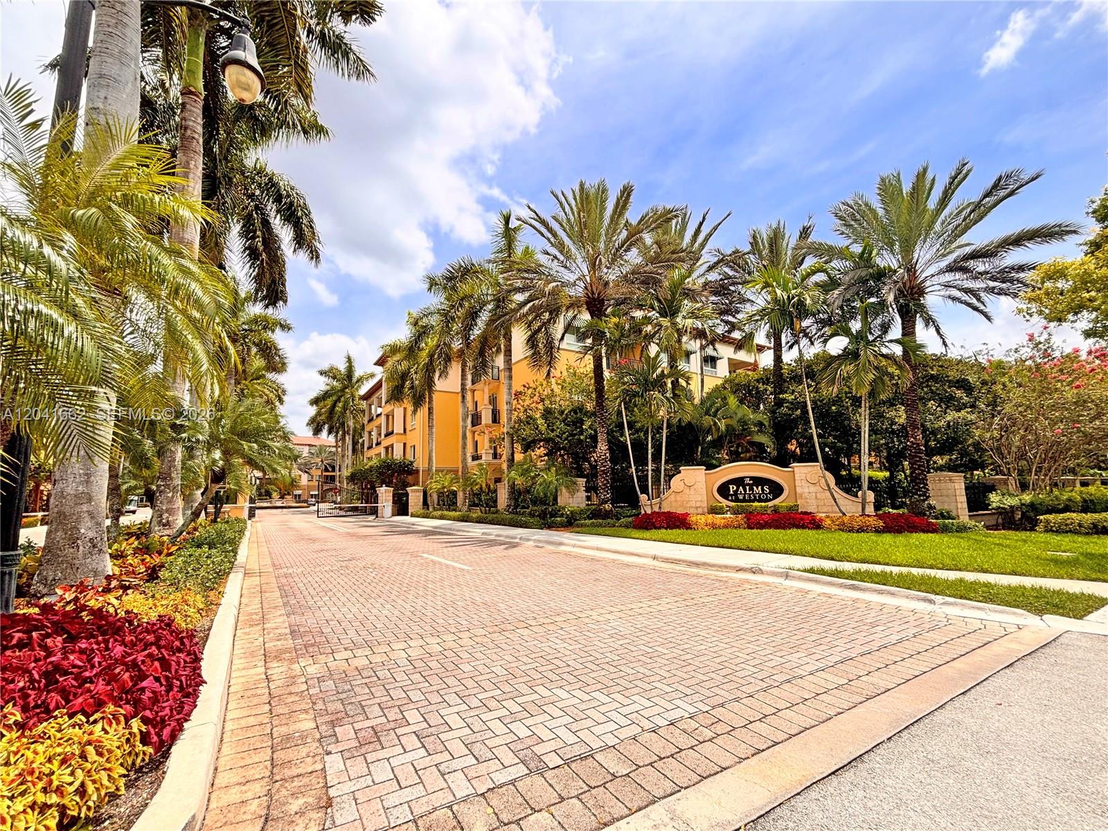 A paved driveway leads to the entrance of The Palms at Weston apartment complex — 16101 Emerald Estates Dr # 155, Weston FL 33331, WESTON, FL