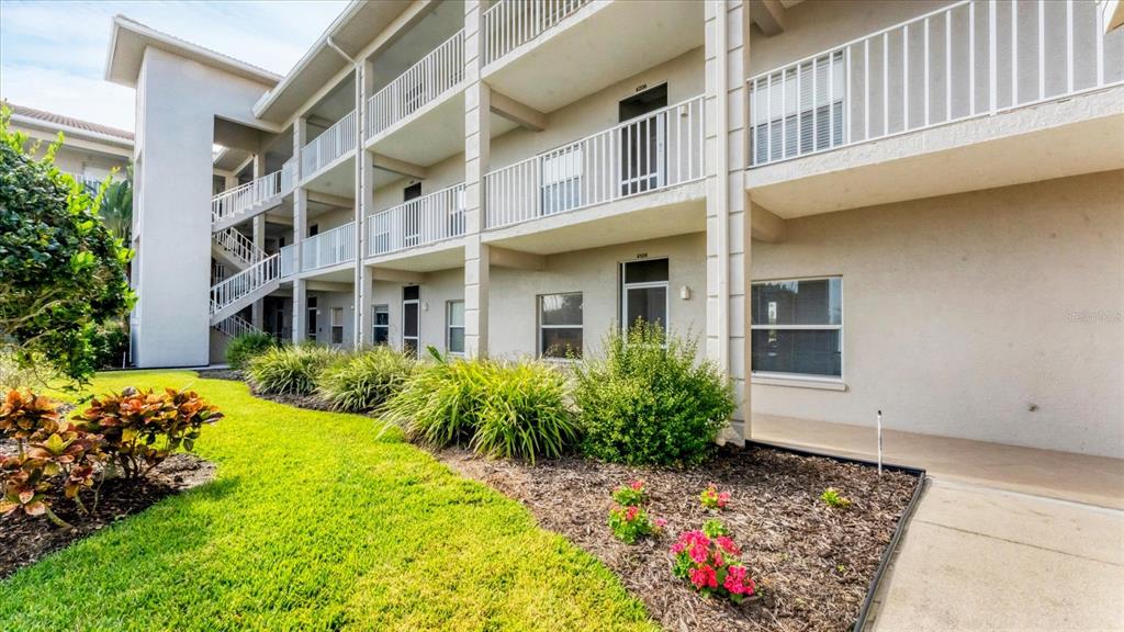 A multi-story apartment building features white railings, exterior staircases, and landscaped garden beds — 9610 CLUB SOUTH CIRCLE UNIT 4106, SARASOTA, FL