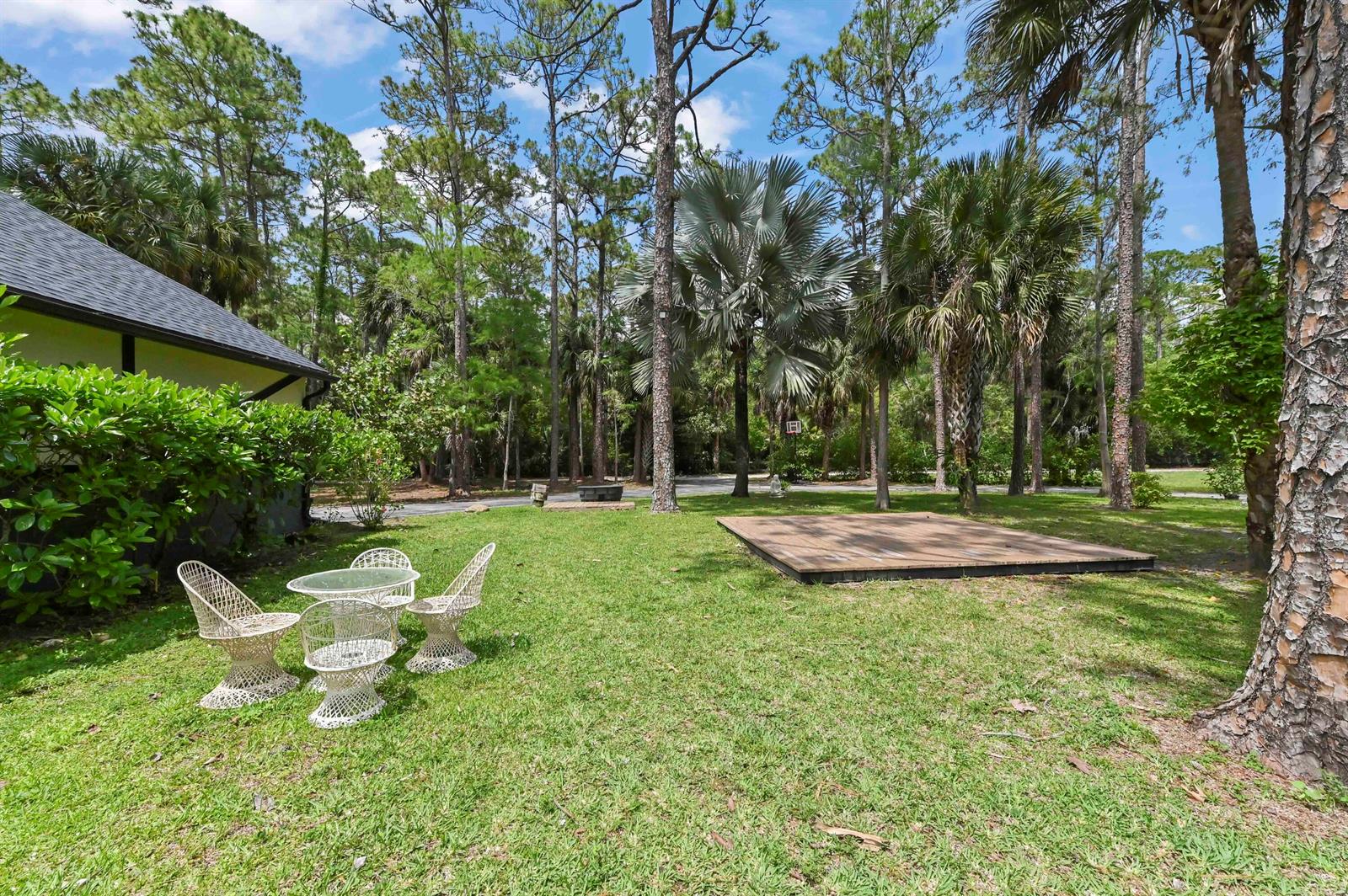 A grassy backyard features a small wooden deck, patio furniture, and surrounding pine trees — 1339 Gallop Drive, Loxahatchee FL 33470, LOXAHATCHEE, FL