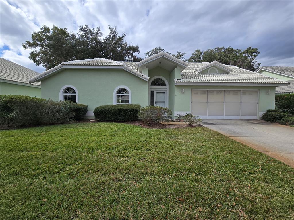 A light green single-story house features a tiled roof, arched windows, and a three-car garage — 719 BALMORAL COURT, INVERNESS, FL