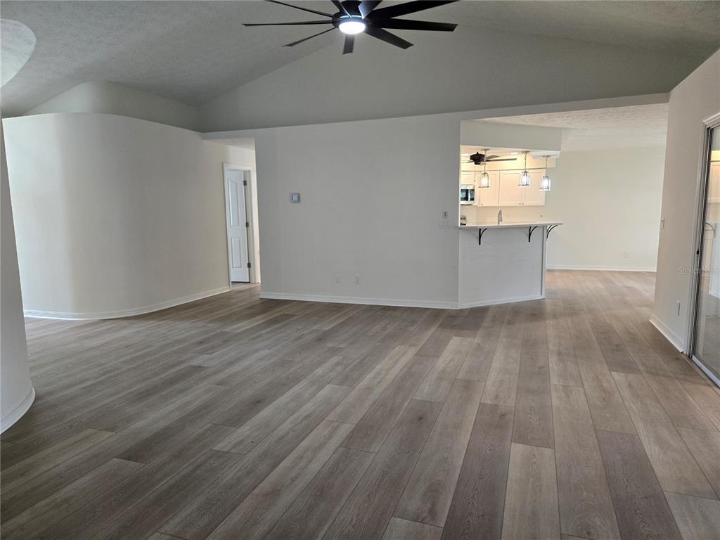 An open-concept living area features light wood-look flooring, a curved wall, and a kitchen island — 719 BALMORAL COURT, INVERNESS, FL