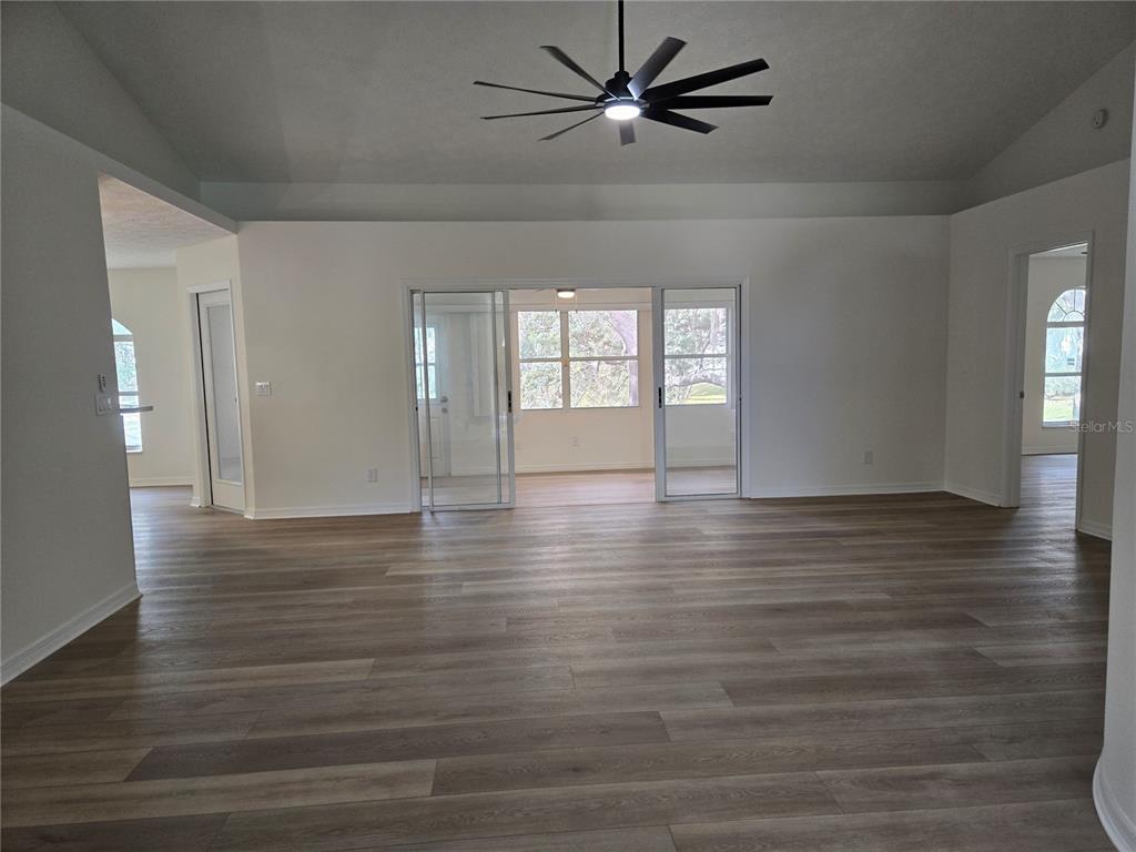 A spacious living room features light wood-look flooring, white walls, and a large ceiling fan — 719 BALMORAL COURT, INVERNESS, FL