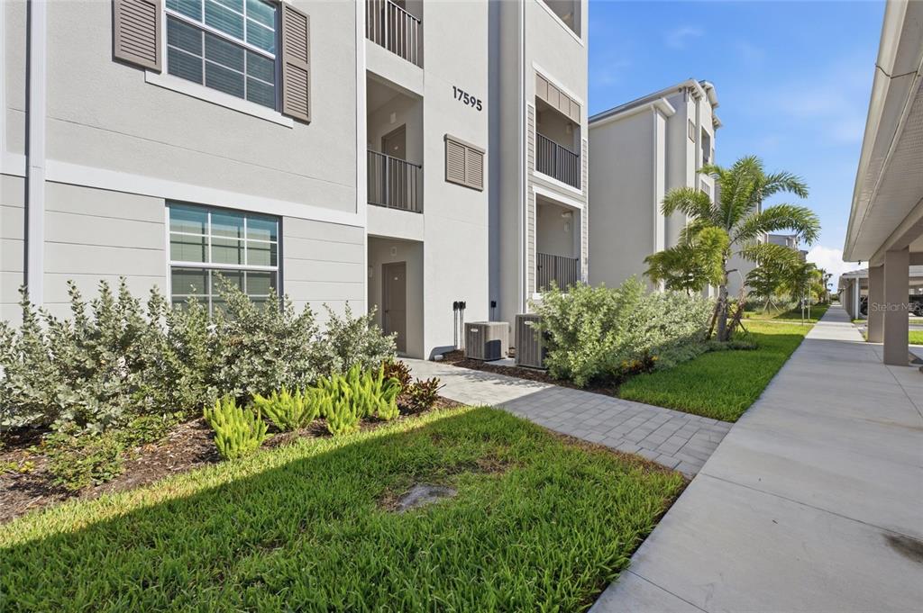 A paved walkway leads to the entrance of a multi-story apartment building with landscaping — 17595 OPAL SAND DRIVE UNIT 302, VENICE, FL